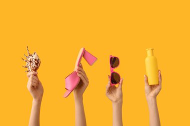 Deniz kabuğu, güneş kremi, güneş gözlüğü ve sarı arka planda topuklu sandalet. Seyahat kavramı.