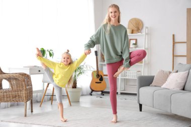 Küçük kızıyla evde yoga yapan sportif bir kadın.