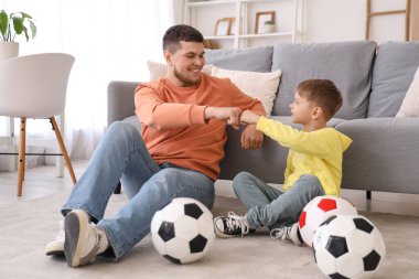 Genç adam ve futbol topları olan küçük oğlu oturma odasında yumruk tokuşturuyorlar.
