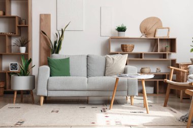 Kanepe, raf üniteleri ve beyaz duvarın yanındaki ev bitkilerinin olduğu rahat bir oturma odası.