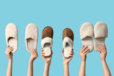 Mavi arka planda farklı terlikler tutan kadın eller.