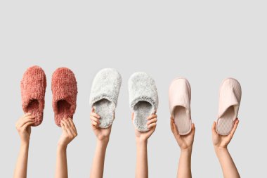 Beyaz arka planda farklı terlikler tutan kadın eller.