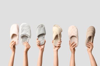 Beyaz arka planda farklı terlikler tutan kadın eller.