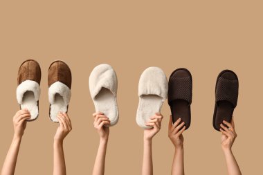 Bej arka planda farklı terlikler tutan kadın eller.