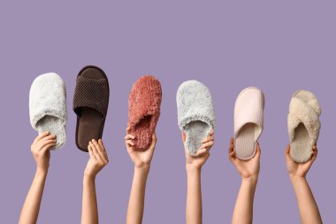 Leylak arka planında farklı terlikler tutan kadın eller.