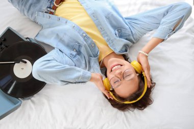 Kulaklığı ve pikabı olan genç bir kadın yatak odasında yatıyor.