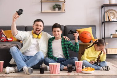 Küçük oğlu ve üzgün kızıyla evde video oyunu oynayan mutlu bir baba.