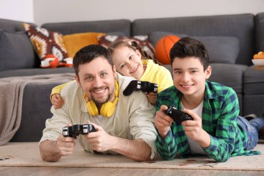 Mutlu baba ve küçük çocukları evde yerde video oyunu oynuyorlar.