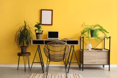 Ofiste sarı duvarın yanında dizüstü bilgisayarı ve bitkileri olan modern bir iş yeri.