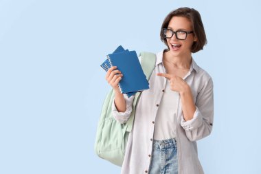 Sırt çantasıyla beyaz arka plandaki defterlere bakan şaşırmış kız öğrenci.