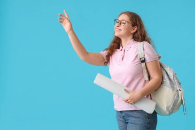 Sırt çantalı ve mavi arka planda el sallayan mutlu bayan öğrenci.