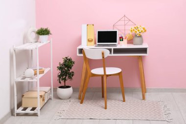 Rafa kaldırma ünitesi ve işyeri. Bir buket narsisli çiçek, kırtasiye ve dizüstü bilgisayar şık bir ofiste pembe duvarın yanında.