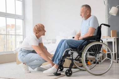 Olgun bir kadın, hasta kocasına tekerlekli sandalyede yardım ediyor.