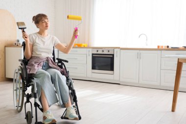 Tekerlekli sandalyedeki genç kadın evde boya fırçası ve silindirle geziyor.