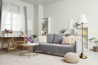 Kanepe, masa ve vazolarda leylak çiçekleriyle aydınlık oturma odasının içinde.