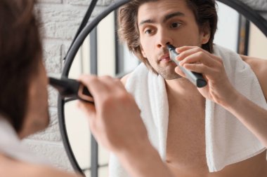 Genç sakallı adam banyoda burun kıllarını kesiyor.