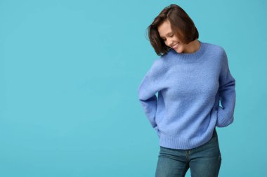 Mavi arka planda şık süveter giyen güzel genç bir kadın.