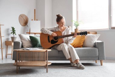 Oturma odasındaki kanepede gitar çalan genç kadın.
