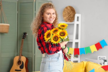 Evinde bir buket ayçiçeğiyle mutlu genç bir kadın. Junina festivali.
