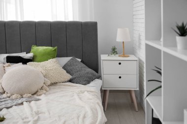 Yatak odasındaki rahat yatağın yanında lamba olan komodin.