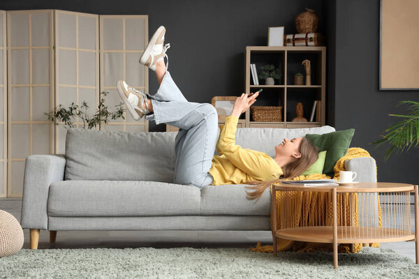 Young woman using mobile phone on grey sofa in living room