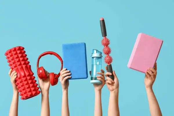 Female hands with foam roller, yoga blocks, sports water bottle, roller massager stick and headphones on blue background