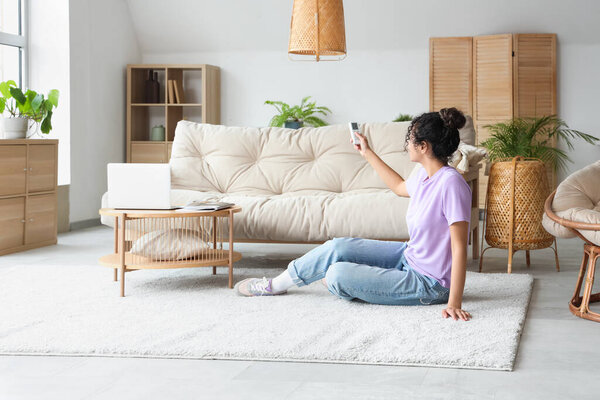 Young African-American woman turning on air conditioner at home