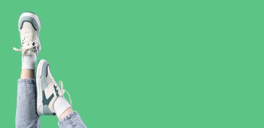 Legs of young woman in stylish sneakers on green background with space for text