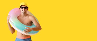 Sarı zemin üzerinde şişirilebilir halkası olan çekici genç bir adam ve metin için yeri var.