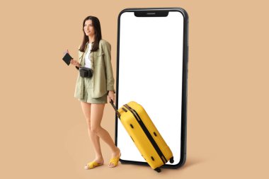 Female tourist with luggage and big smartphone on beige background