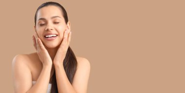 Beautiful young woman massaging her face on beige background with space for text