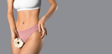 Young woman in panties and with gerbera flower on grey background with space for text