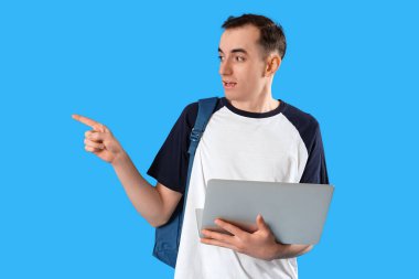 Male student with laptop pointing at something on blue background