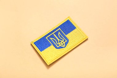 Üç çatallı askeri rozet ve bej arka planda Ukrayna bayrağı.