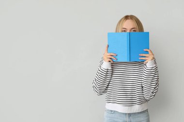 Beautiful young woman with book on grey background