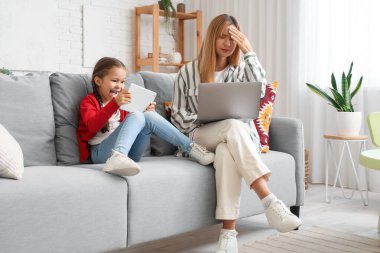 Çalışan genç bir kadın evde tablet bilgisayarlı gürültücü küçük kızı yüzünden stresli.