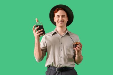 Yeşil arka planda şişe ve bir bardak viskiyle genç bir barmen.