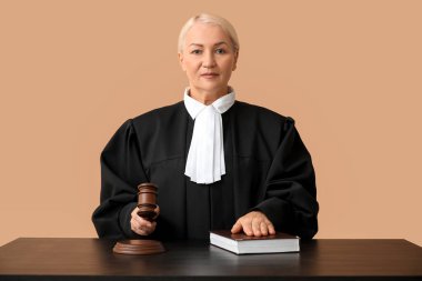 Kahverengi arka planda tokmak ve kitap bulunan olgun kadın yargıç.