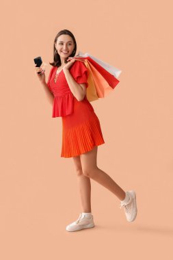 Kredi kartı, cep telefonu ve bej arka planda alışveriş torbaları olan genç bir kadın.