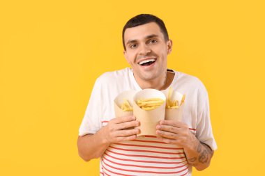 Sarı arka planda patates kızartması olan mutlu genç adam.