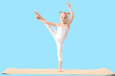 Sevimli küçük kız mavi arka planda jimnastik yapıyor.