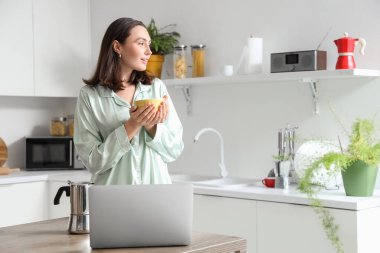 Modern mutfakta gayzer kahve makinesi, bir fincan espresso ve dizüstü bilgisayarı olan güzel bir kadın.