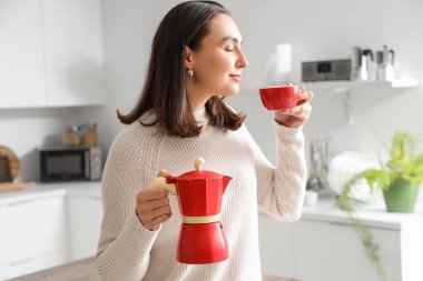 Pretty young woman enjoying aroma of fresh espresso from geyser coffee maker in modern kitchen, closeup