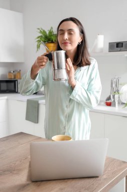 Pretty young woman enjoying aroma of fresh espresso from geyser coffee maker in modern kitchen