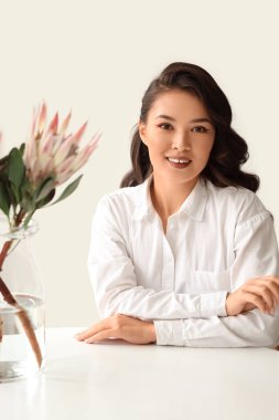 Beyaz duvarın yanındaki masada güzel protea çiçekli genç Asyalı kadın.