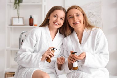 Annesiyle banyodan sonra krem süren genç bir kadın.