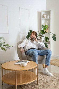 Evdeki yumuşak koltukta cep telefonuyla konuşan yakışıklı adam.