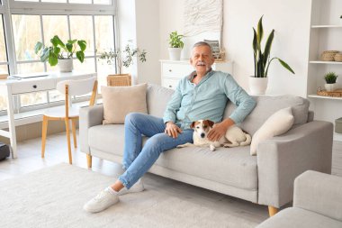 Evdeki kanepede oturan tatlı Jack Russell teriyeri olan olgun bir adam.