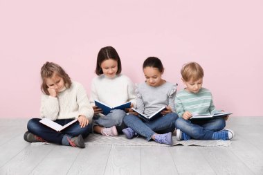 Pembe duvarın yanında oturmuş kitap okuyan küçük çocuklar.