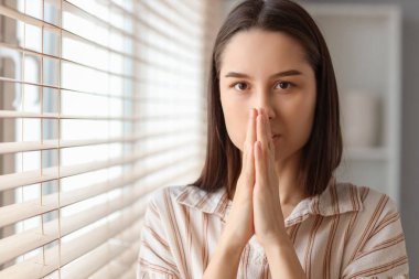 Evdeki pencerenin yanında dua eden güzel genç bir kadın.